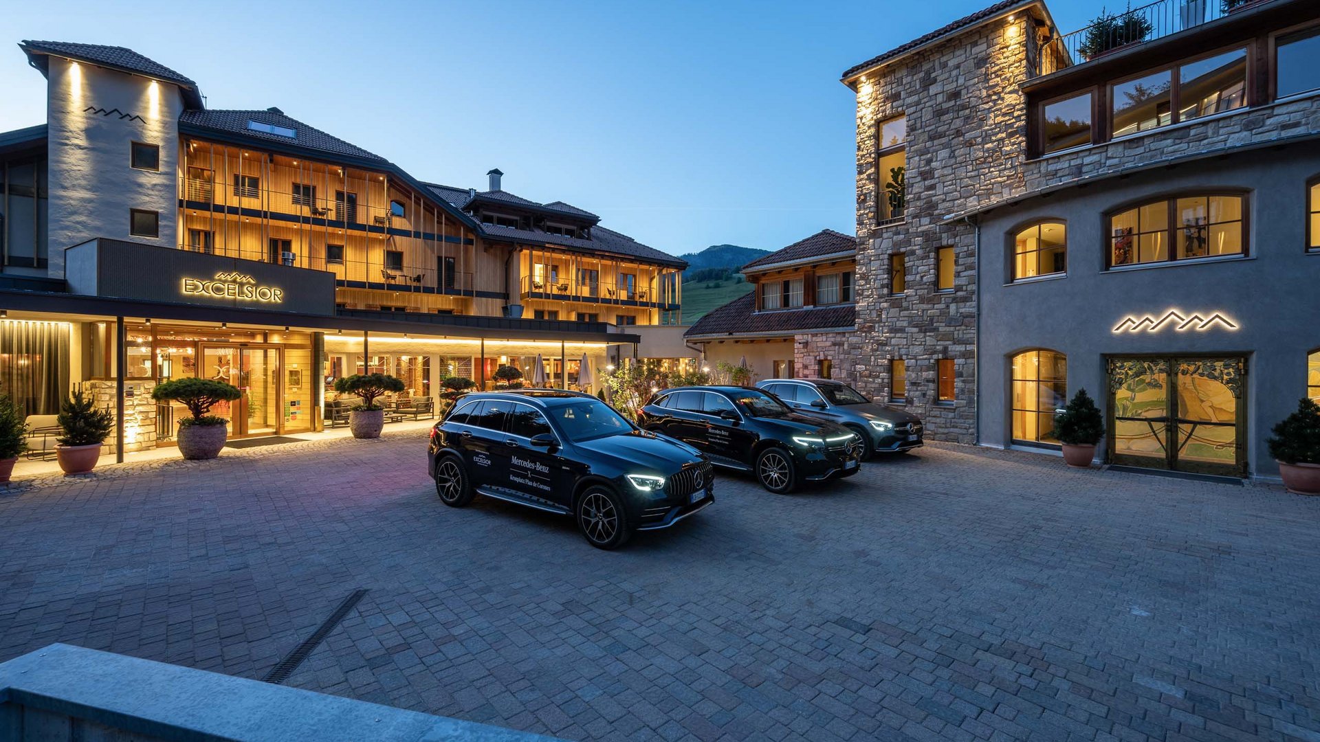 Drei geparkte schwarze Mercedes vor dem beleuchteten Hotel Excelsior am Abend